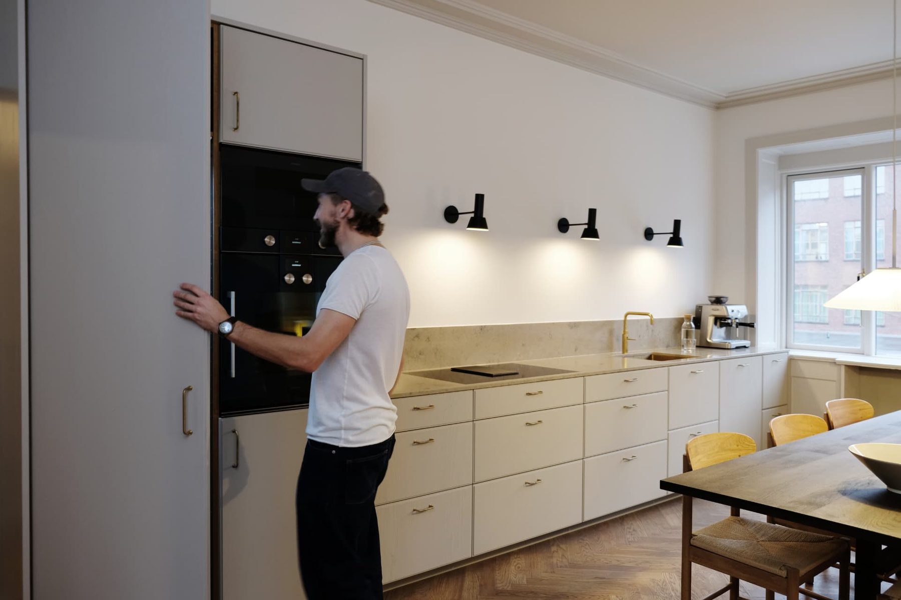 Køkken med lyse fronter, messinggreb, stenbordplade og sildebensgulv