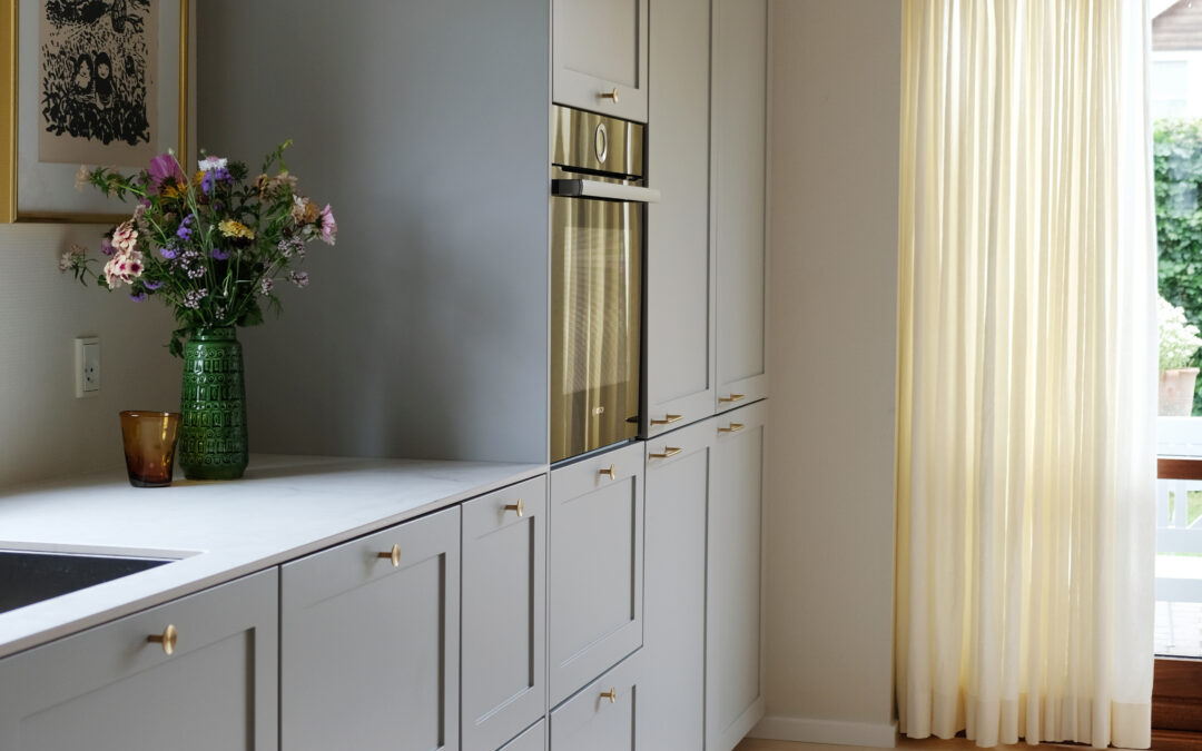 Gråt køkken med messinggreb, hvide bordplader og blomsterdekoration – inspiration til hvilken farve køkken man skal vælge for et tidløst udtryk.