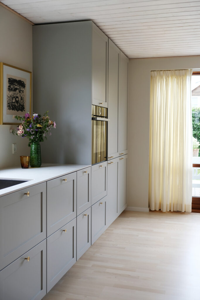 Gråt køkken med messinggreb, hvide bordplader og blomsterdekoration – inspiration til hvilken farve køkken man skal vælge for et tidløst udtryk.