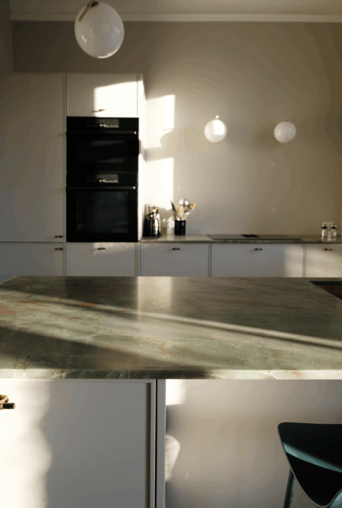 Lyst køkken med grøn marmorbordplade og hvide fronter – eksempel på farvekombinationer, når man overvejer, hvilken farve køkken man skal vælge.