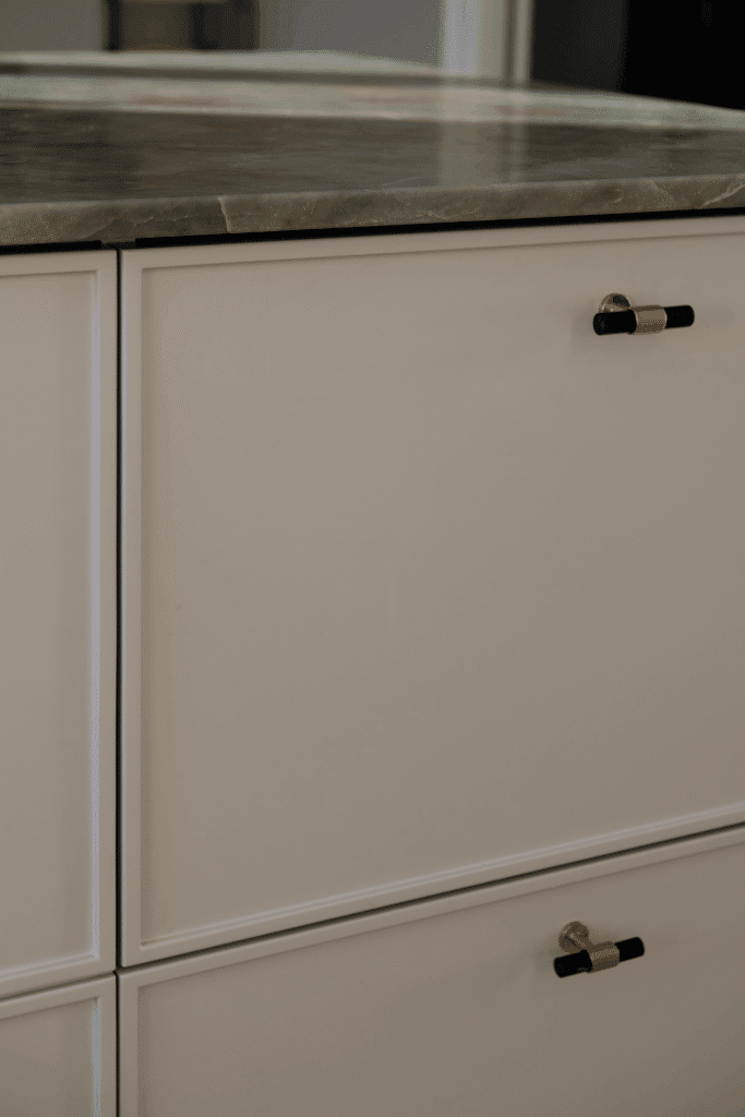 Nærbillede af lyse køkkenlåger med sorte og messingfarvede greb samt grøn marmorbordplade – inspiration til, hvilke køkkenlåger holder bedst over tid.