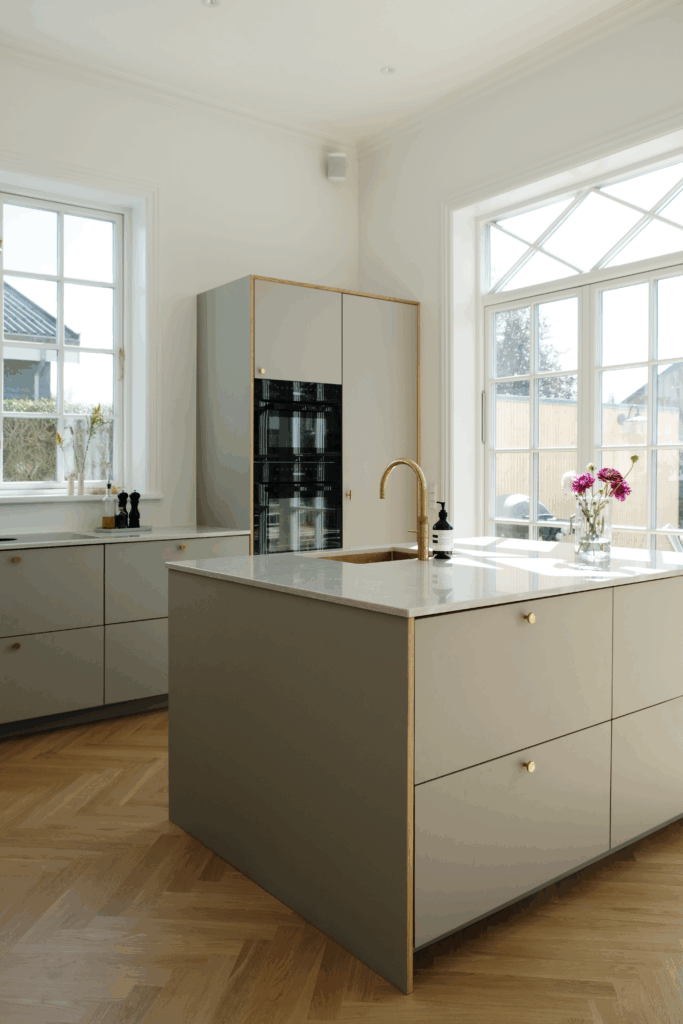 Lyst og moderne køkken med grå fronter, messinggreb og køkkenø – elegant inspiration til nyt køkken i nordisk design.