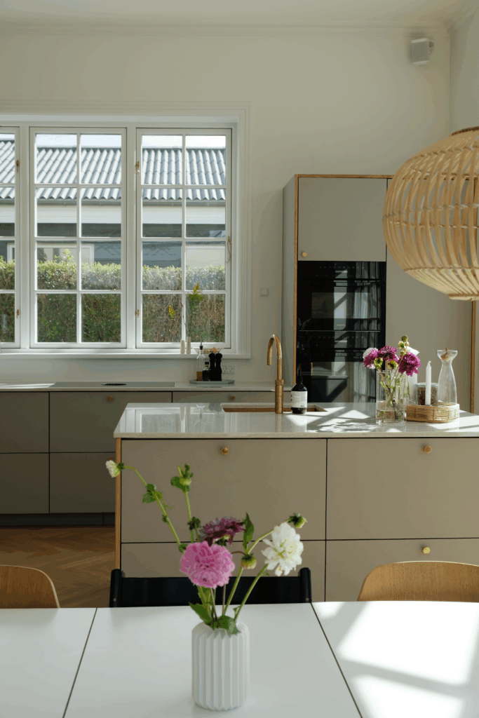 Lyst og moderne køkken med grå fronter, messingarmatur og blomster på bordet – eksempel på processen og resultatet, når man overvejer, hvor lang tid tager det at lave et nyt køkken.