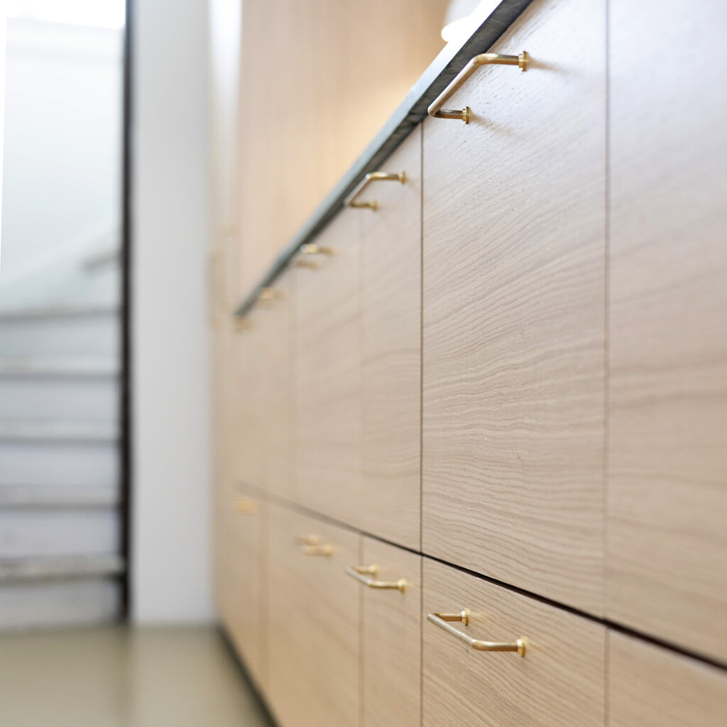 Nærbillede af elegante køkkenskabe i egetræ med messinggreb, der viser detaljerne i en stilfuld renovering af gammelt køkken.