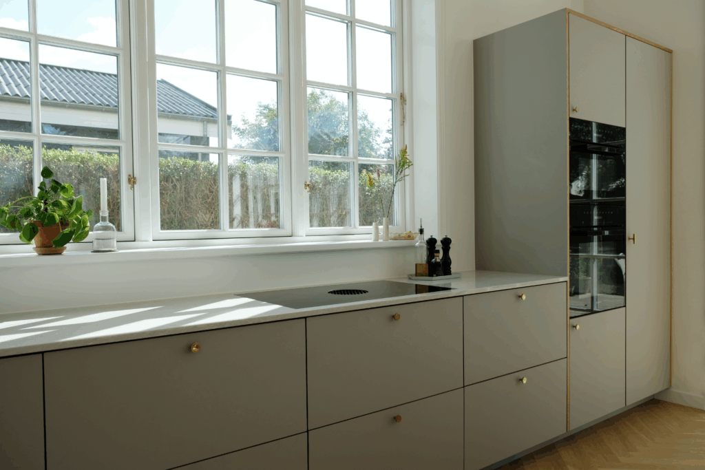 Elegant køkken i afdæmpet grøn nuance med messinggreb og store vinduer, der giver naturligt lys og masser af grønt køkken inspiration.