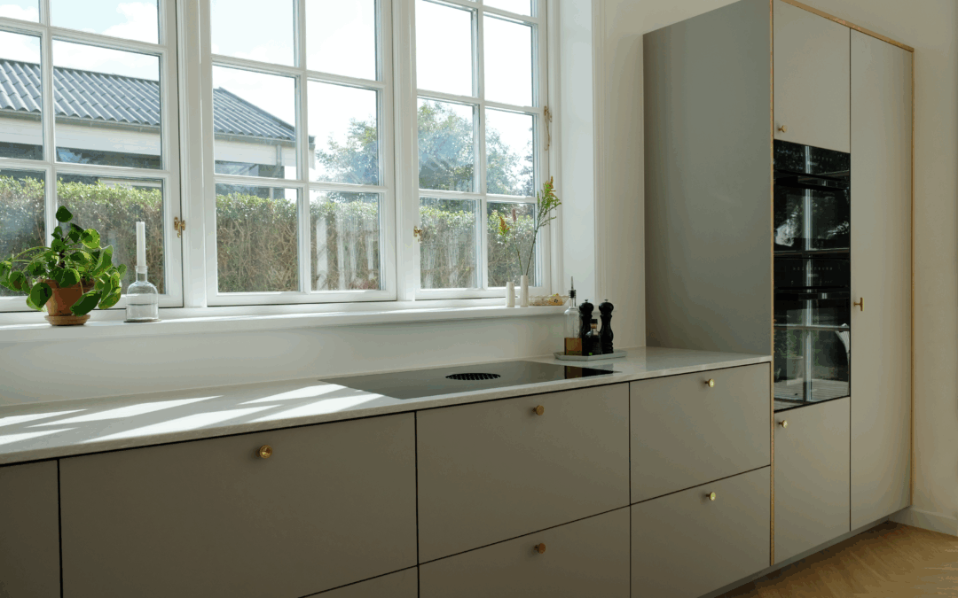 Elegant køkken i afdæmpet grøn nuance med messinggreb og store vinduer, der giver naturligt lys og masser af grønt køkken inspiration.