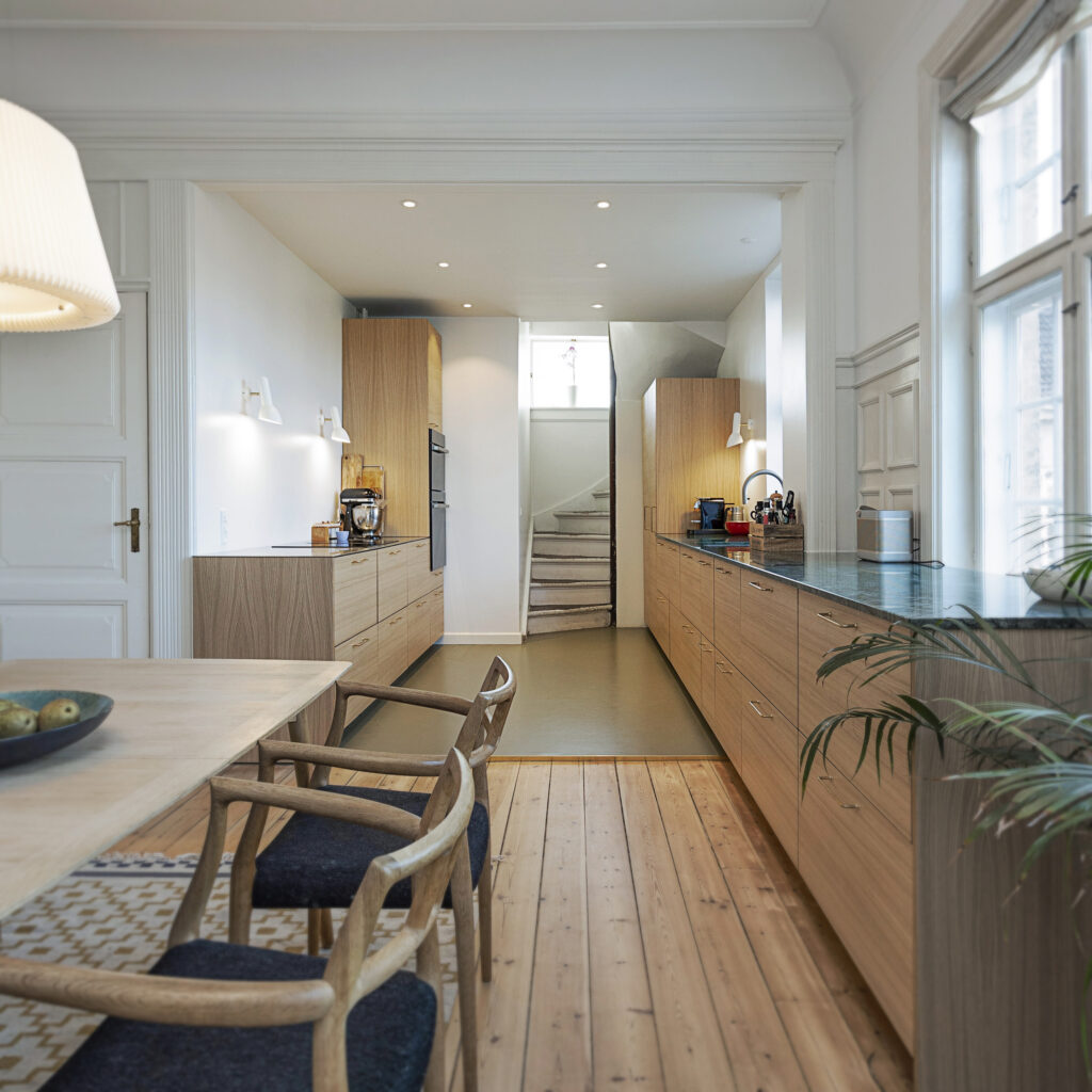 Elegant langt køkken i naturtræ med grøn bordplade og spiseplads i forlængelse, der giver inspiration til hvad koster et nyt køkken i høj kvalitet.