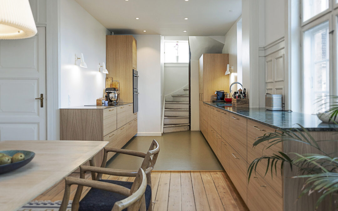 Elegant langt køkken i naturtræ med grøn bordplade og spiseplads i forlængelse, der giver inspiration til hvad koster et nyt køkken i høj kvalitet.