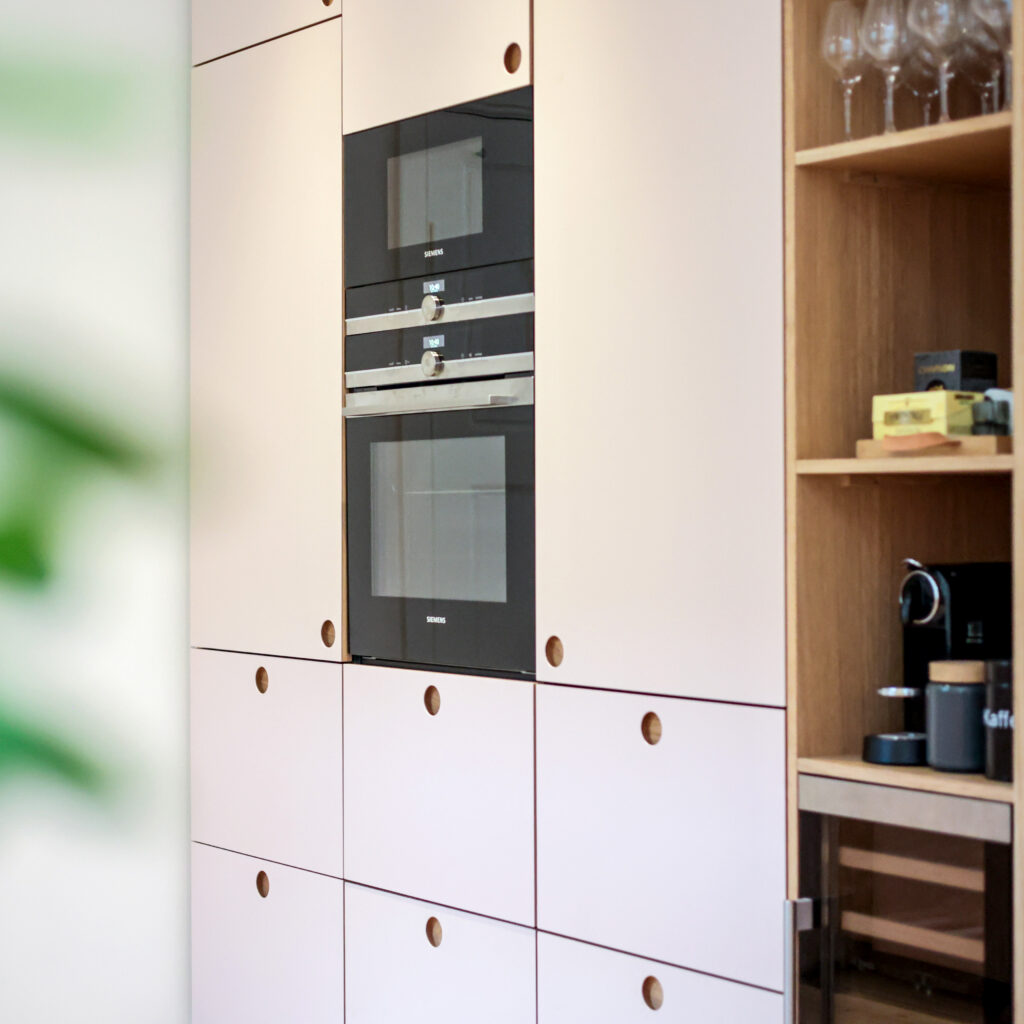 Elegant beige køkken med integrerede ovne og runde trægreb, der giver et roligt og tidløst udtryk – perfekt som beige køkken inspiration.