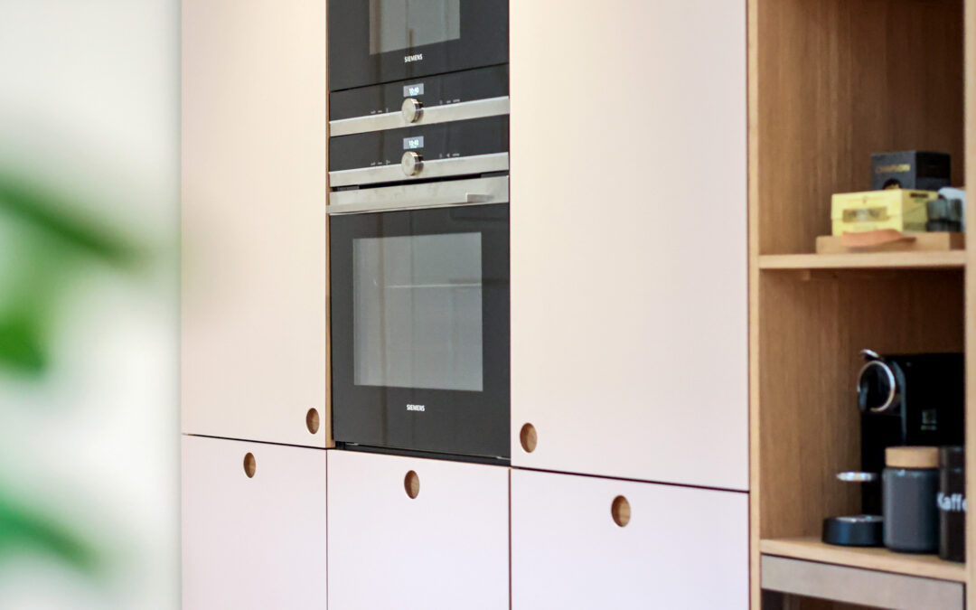 Elegant beige køkken med integrerede ovne og runde trægreb, der giver et roligt og tidløst udtryk – perfekt som beige køkken inspiration.