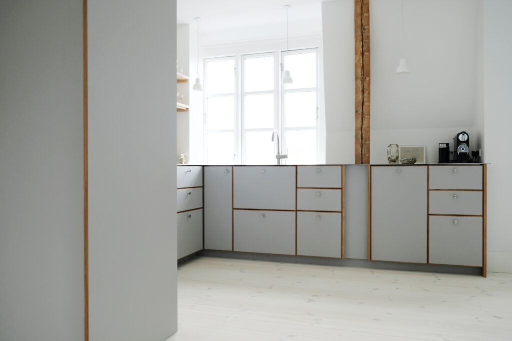 Stilrent gråt køkken med trædetaljer, lyse gulve og store vinduer, der giver et roligt og moderne udtryk – perfekt som gråt køkken inspiration.