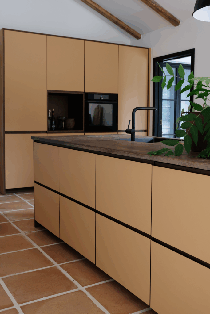 Nærbillede af køkkenø og skabe i dæmpet gul nuance med træbordplade, perfekt til gult køkken inspiration med naturlige materialer.