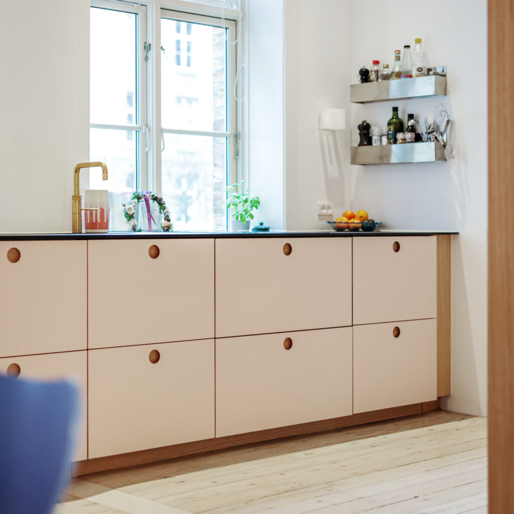 Lyst beige køkken med messingarmatur, sorte bordplader og naturligt lys fra vinduet – et smukt eksempel på beige køkken inspiration med nordisk stil.