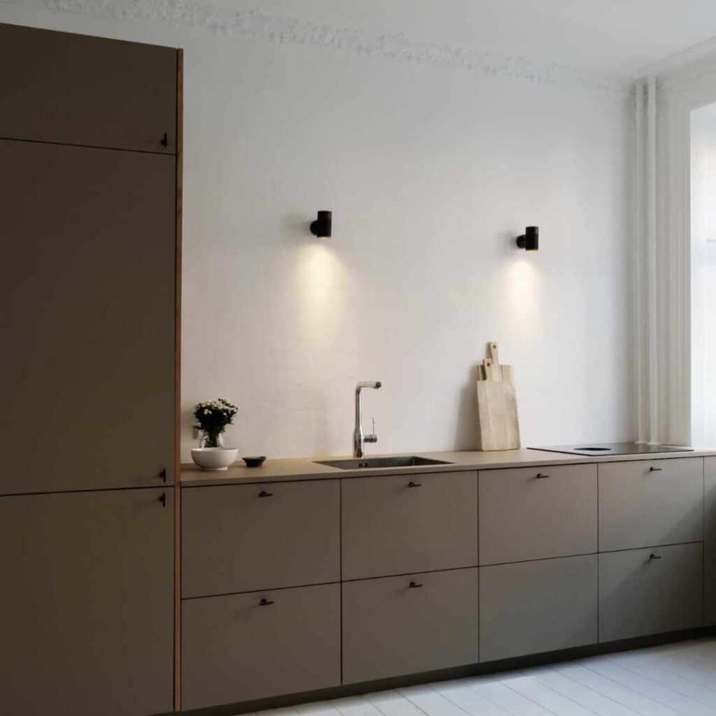Indretning af lille køkken med minimalistiske skabe, vægbelysning og god arbejdsplads.