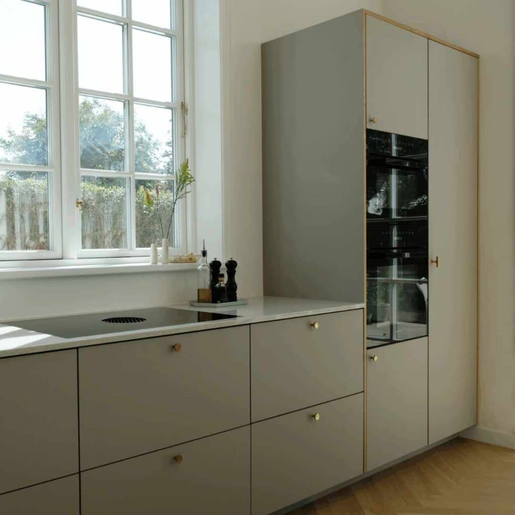 Olivengrøn køkken med elegante fronter, høje skabe, integrerede ovne og stort vinduesparti.