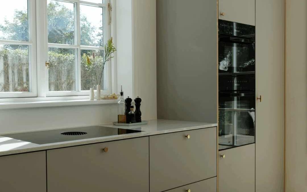 Olivengrøn køkken med elegante fronter, høje skabe, integrerede ovne og stort vinduesparti.