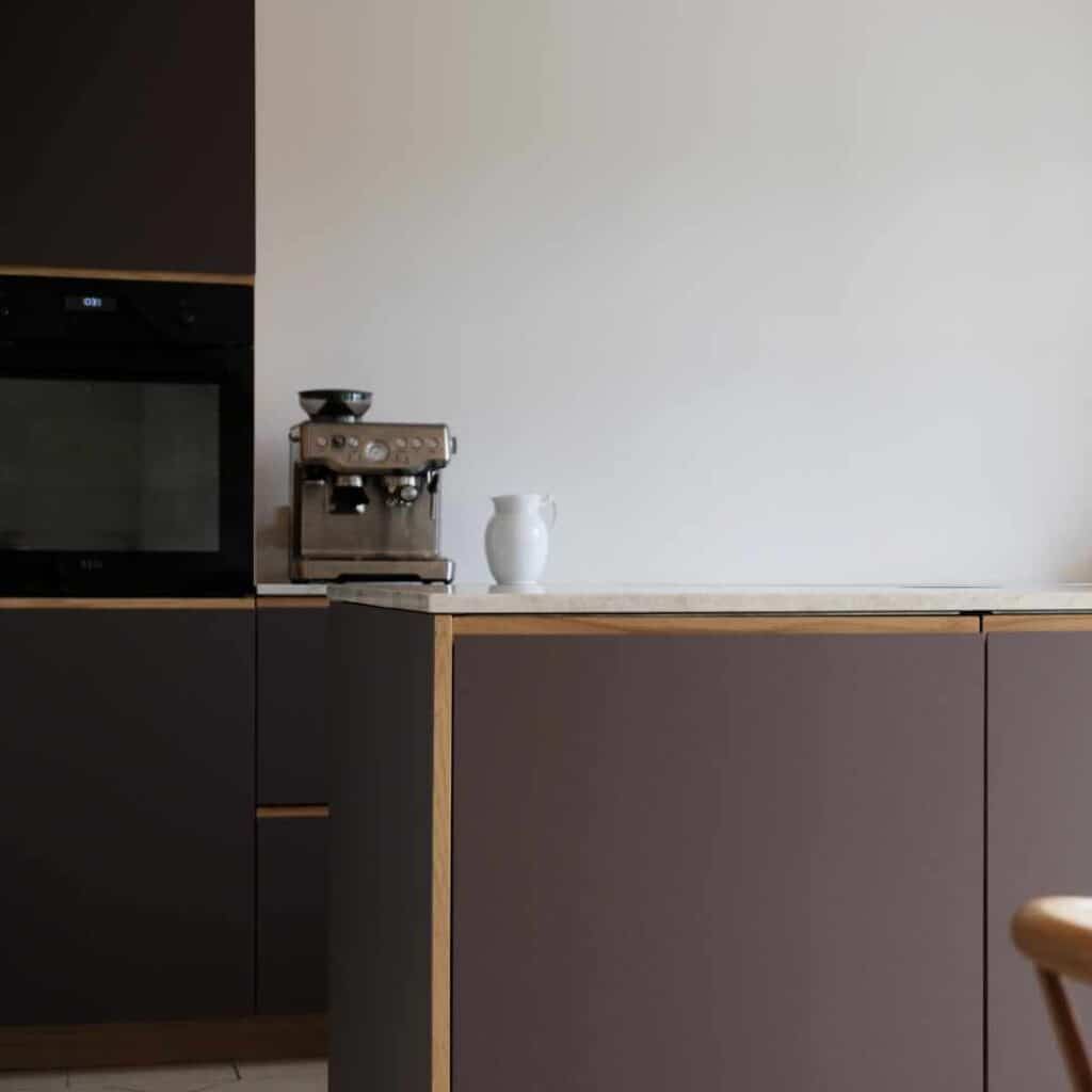 Mørkt køkken med elegante mørke fronter og lyse bordplader, der skaber et eksklusivt og moderne udtryk.