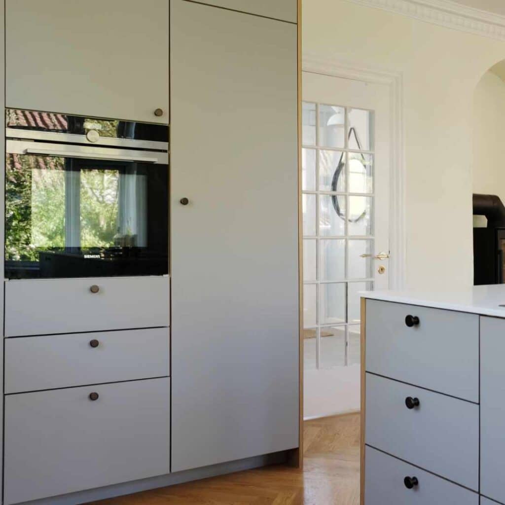 Lysegråt køkken med elegante fronter, sorte greb og et klassisk, tidløst design i lyse omgivelser.