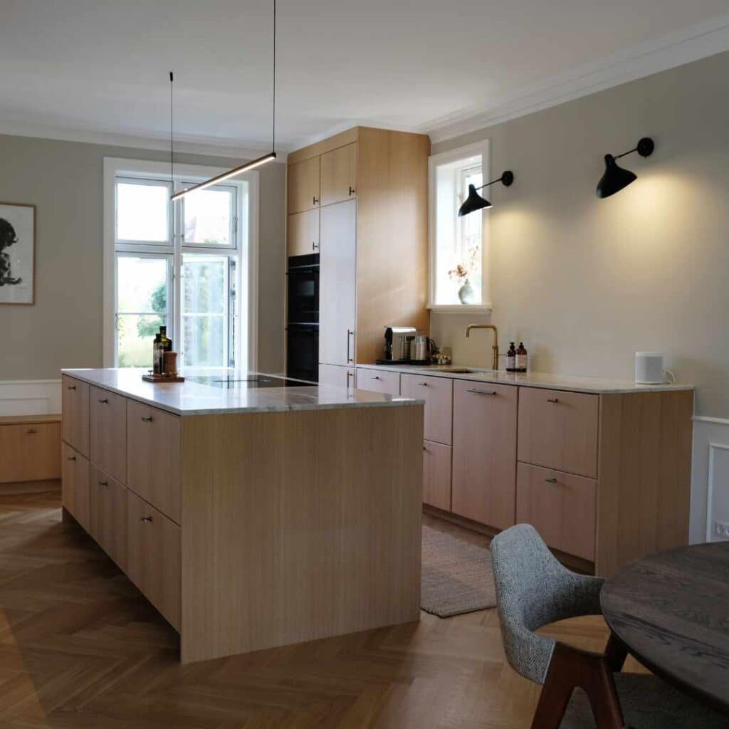 Køkken i lyse træfarver med køkkenø, marmorbordplade og nordisk design.