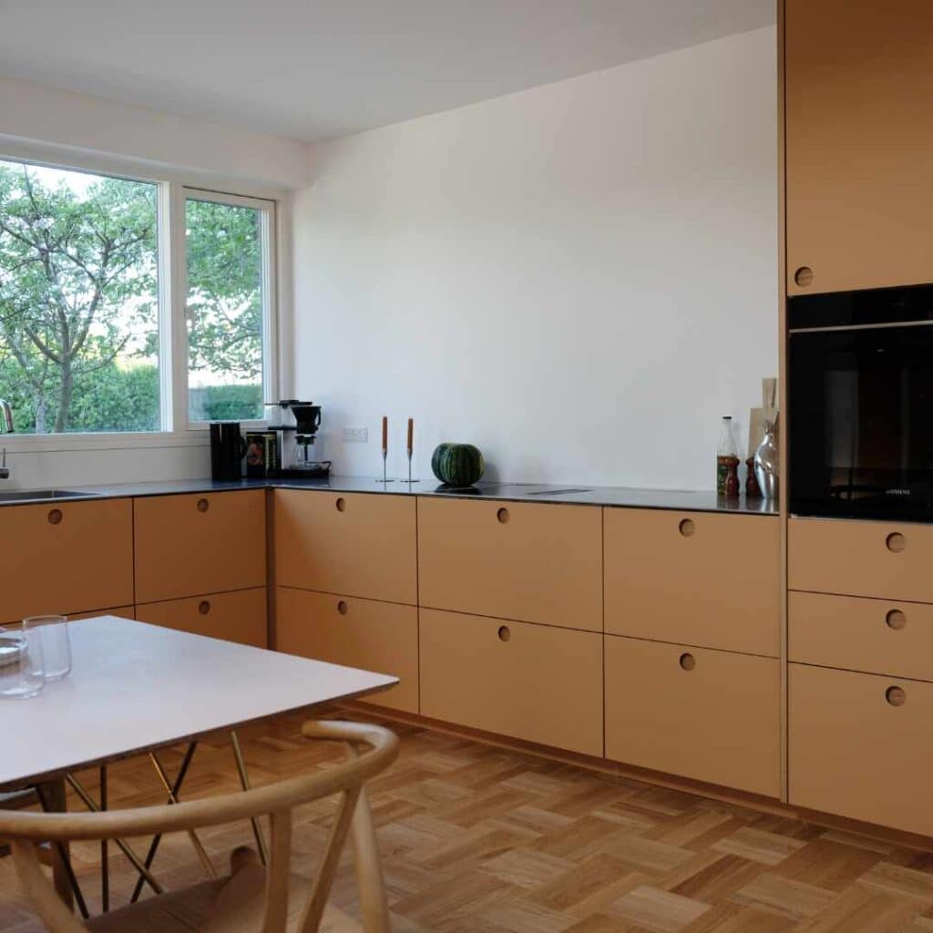 Køkken i varme sandfarver med grebsfrie fronter og moderne, minimalistisk indretning.