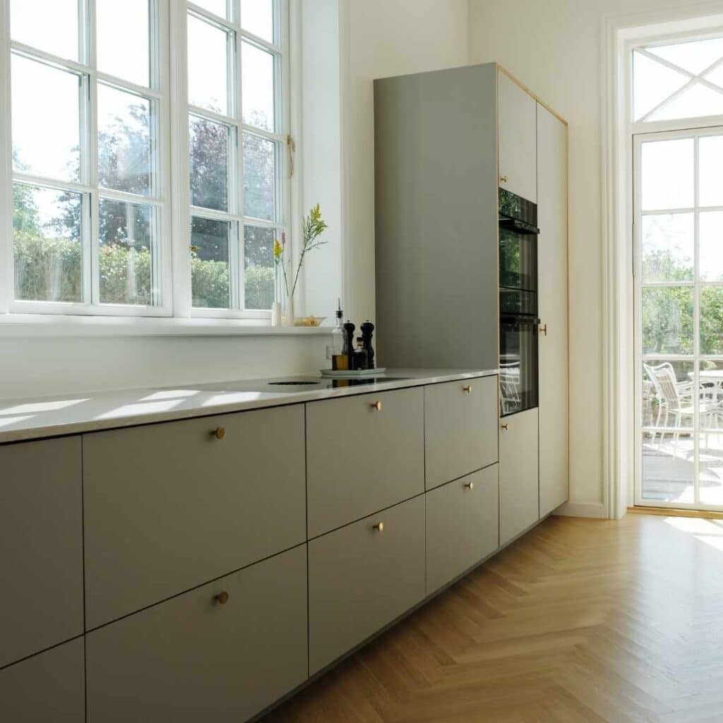 Moderne L formet køkken med lyse fronter, grebsløst design og masser af dagslys.