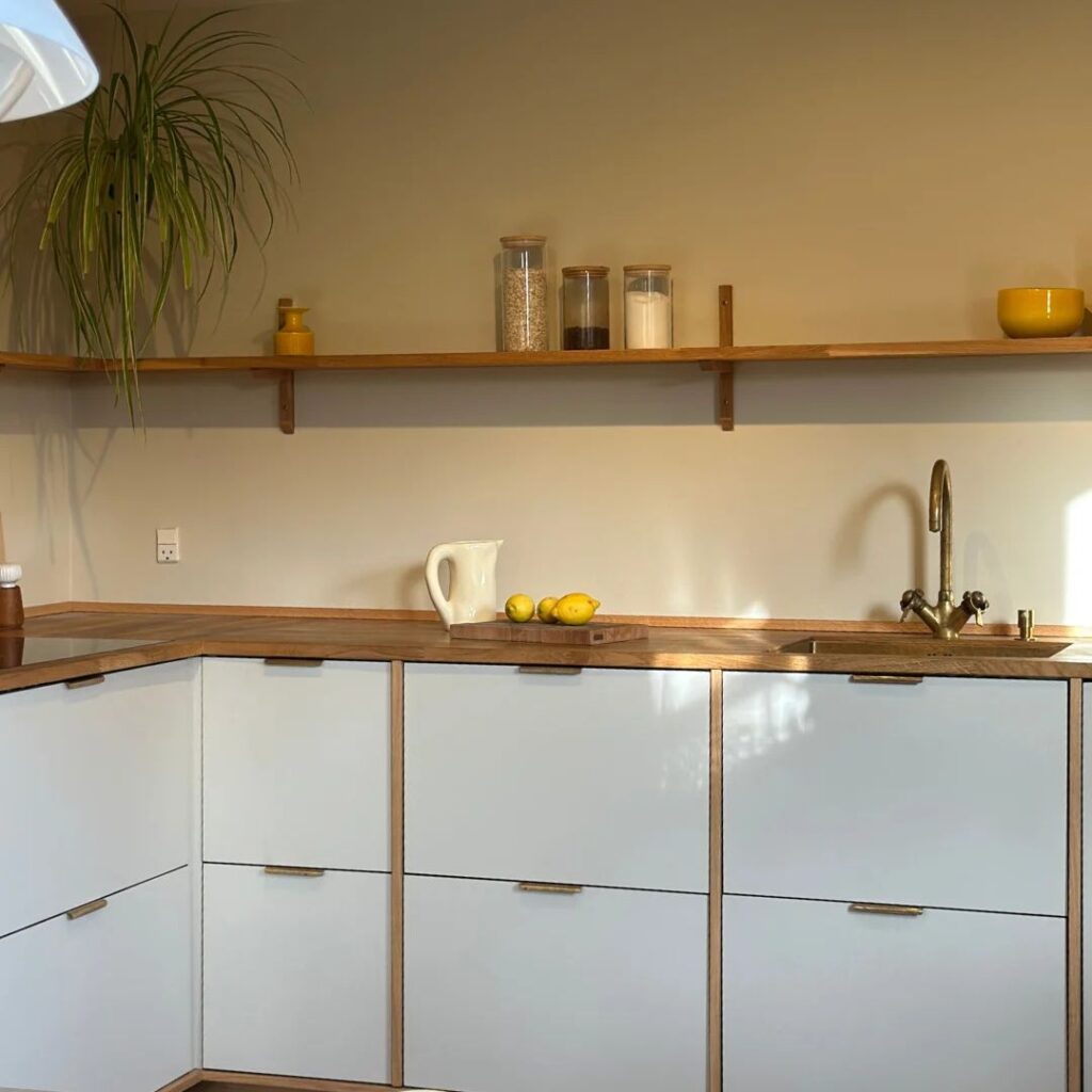 Moderne køkken med hvide fronter, træbordplade, åbne hylder og messingdetaljer.